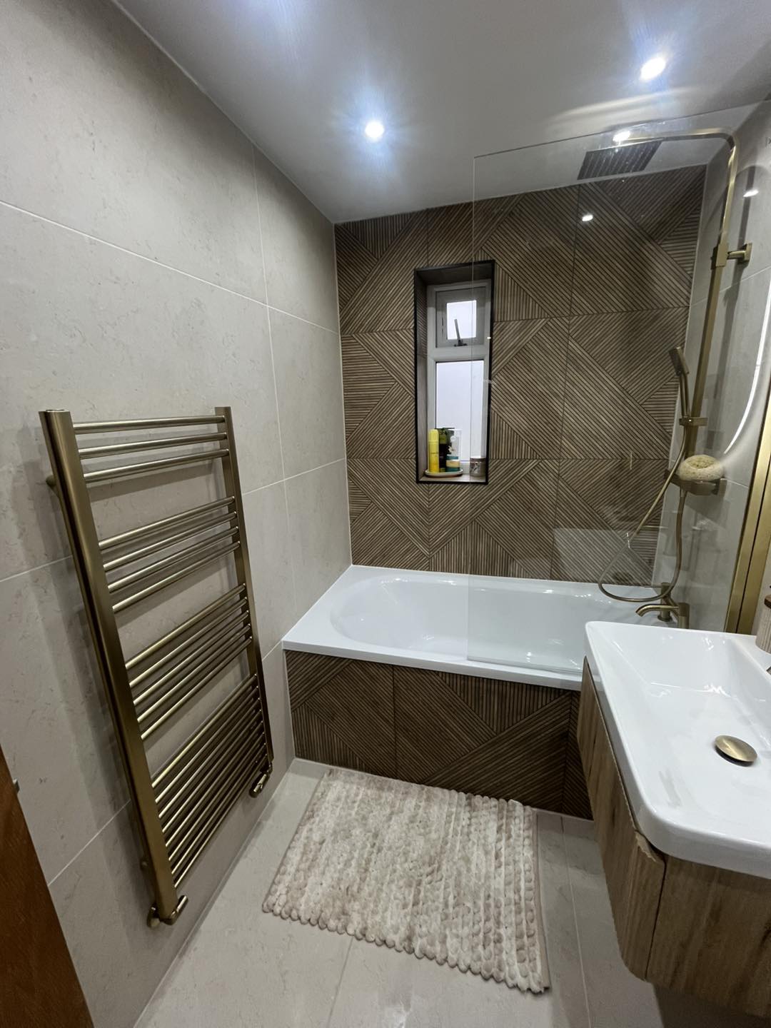 Bathroom after — modern wood-effect feature wall, brushed brass fittings, full-height shower